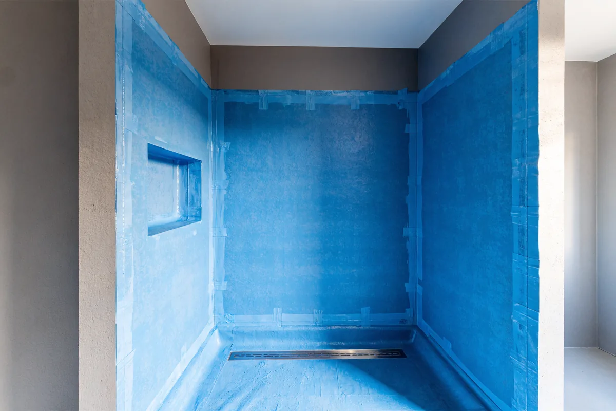 Illustration of a walk-in shower in a Vaughan bathroom renovation coated in a blue waterproofing membrane with taped corners, a membrane-lined niche and a linear drain, before tile